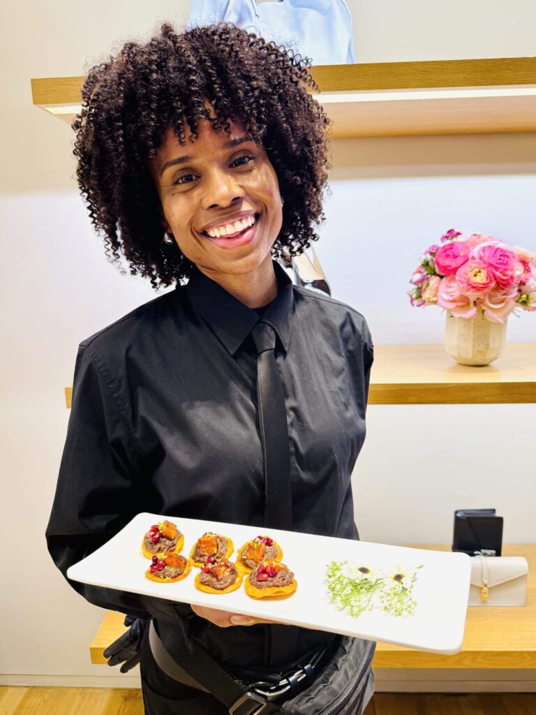 Sweet Basil server smiling while presenting a tray of elegant canapés topped with pomegranate, during a luxury event in New York City.