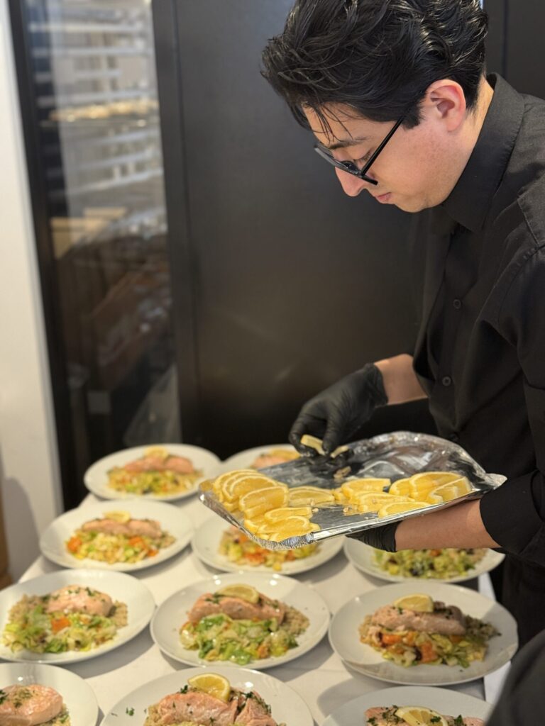 Sweet Basil chef garnishing plated entrees with fresh orange slices during corporate catering prep in New York City.