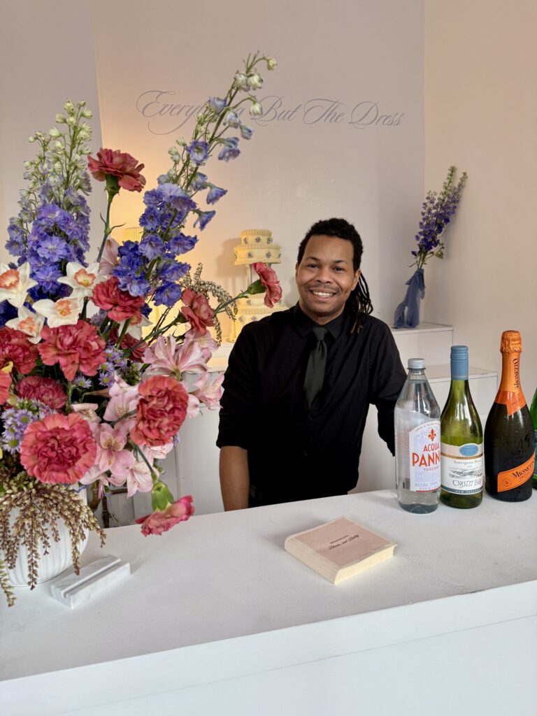 Sweet Basil bartender smiling behind a minimalist white bar with floral arrangements and beverage service, ready for a New York City corporate event.