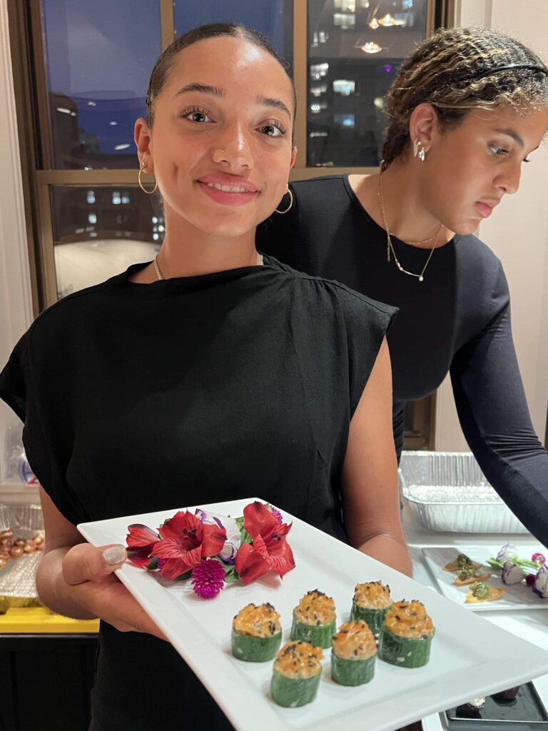 Sweet Basil Catering staff member presenting a white tray with elegantly plated hors d’oeuvres and edible flowers at a New York City corporate event.