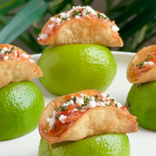 Mini chicken tinga tacos topped with cotija and cilantro served in lime halves.